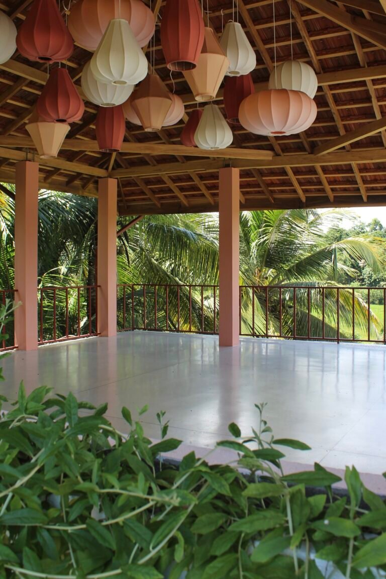 Open-air rooftop space with lanterns under the wooden roof, surrounded by palm trees